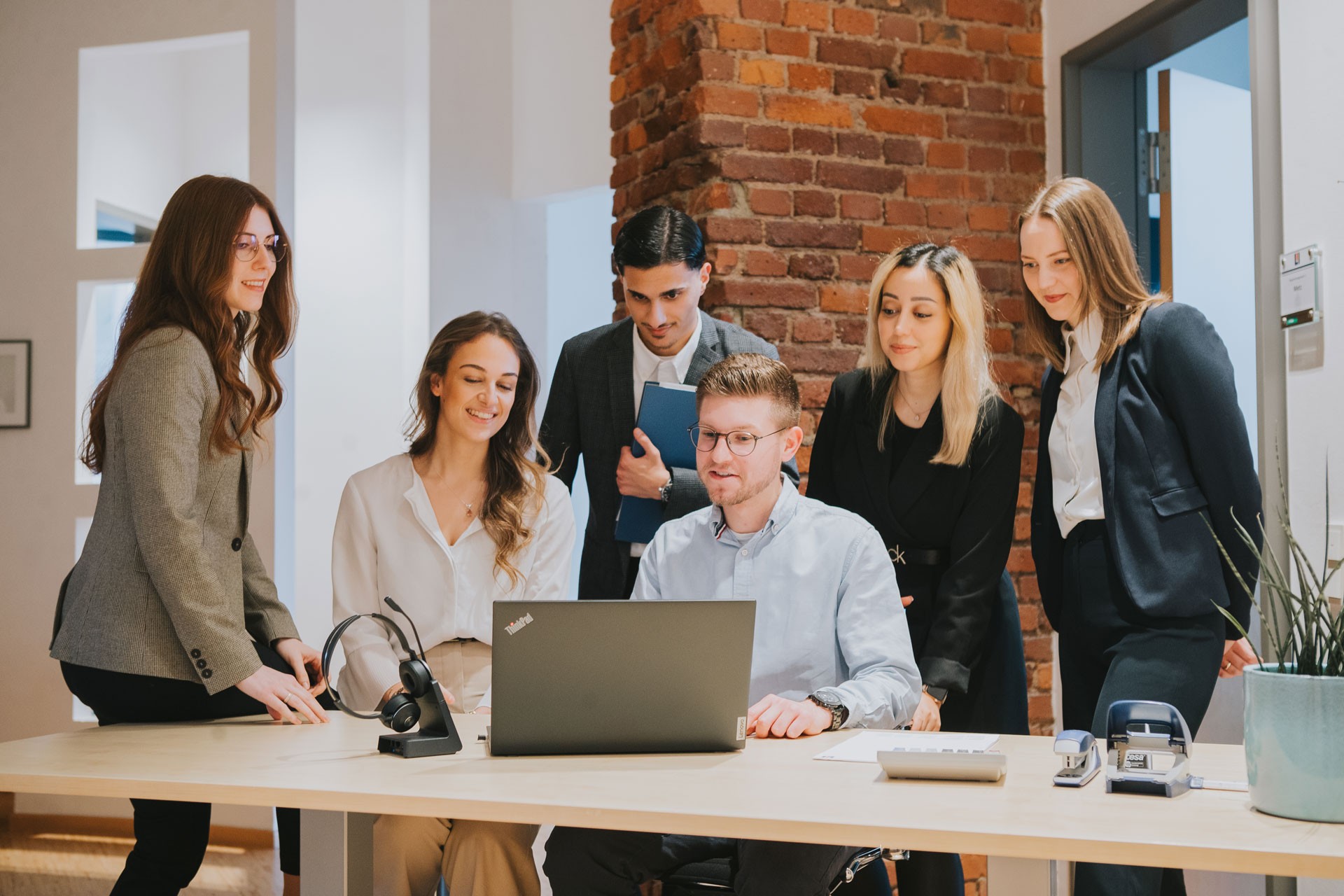 Team steht vor Schreibtisch und schaut in einen Laptop